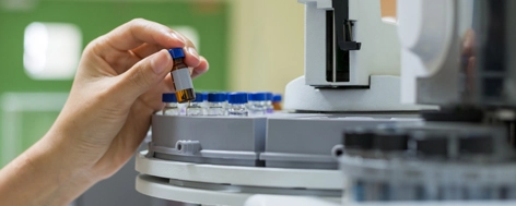 A hand placing a vial sample into a laboratory test machine.