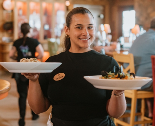 A Bahama Breeze employee carrying plates and smiling