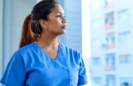 	A nurse looking out a hospital window.