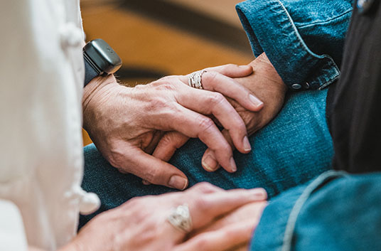 A person with their hands placed on top of a patient's hands to provide comfort
