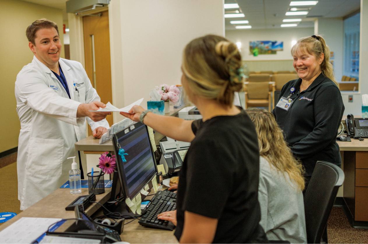 A doctor handing documents to a group of front desk employees.