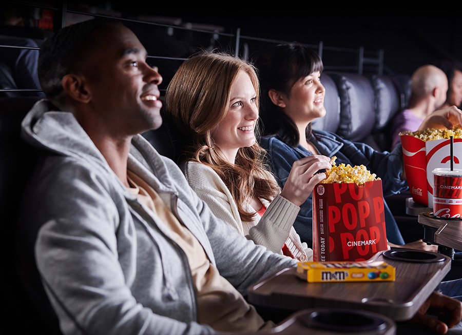 Three people watching a movie at a Cinemark theatre and eating popcorn.