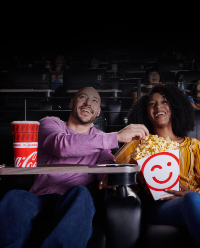 Two people sharing popcorn and watching a movie at a Cinemark theatre.