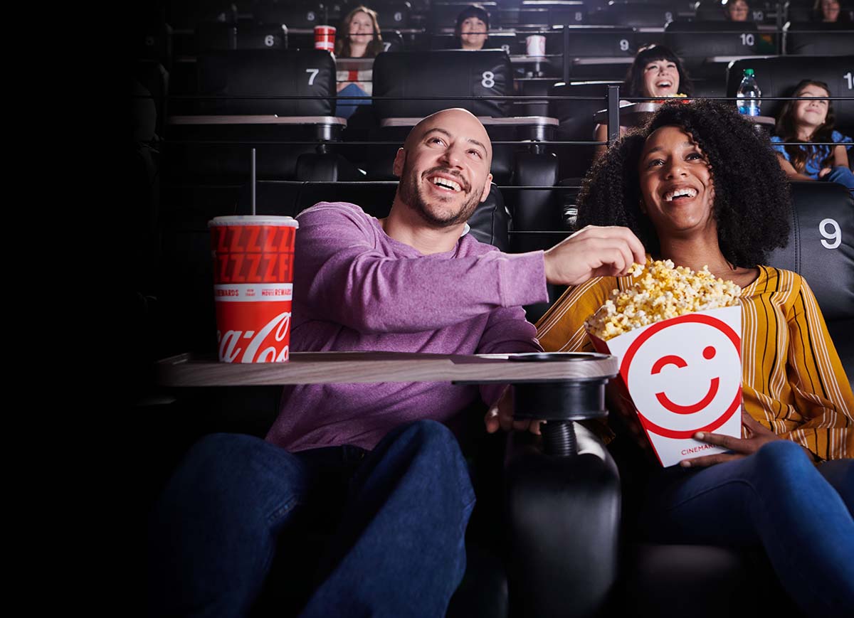 Two people sharing popcorn and watching a movie at a Cinemark theatre.