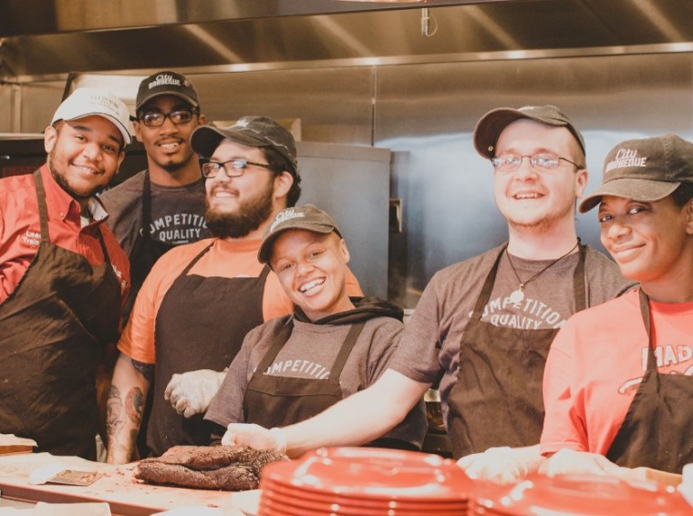 A large group of happy City BBQ teammates working in food prep.