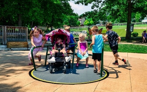 Several children playing on a carousel in a park.