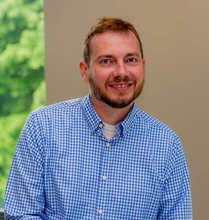 EMH&T employee Matt S. with office wall and window with greenery in background.