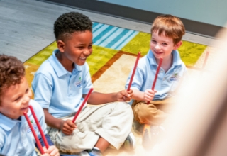 Three children sitting down with drumsticks.