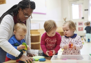 A woman teaching three babies through sensory play.