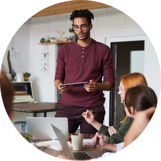 A young executive explains a new project in front of seated colleagues in a conference room.