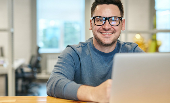 A smiling male social media specialist works on his laptop.