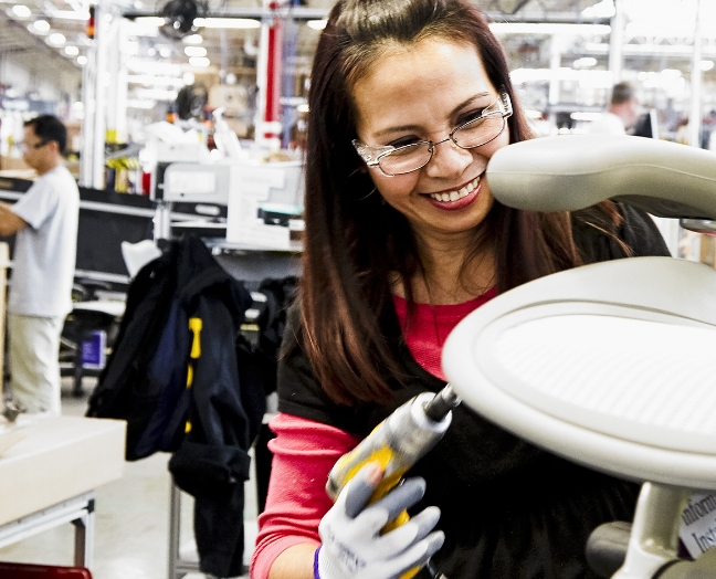  a	A smiling female technical machine operator works on a chair.