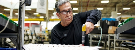  	An older, male upholsterer screws in a chair's padding.