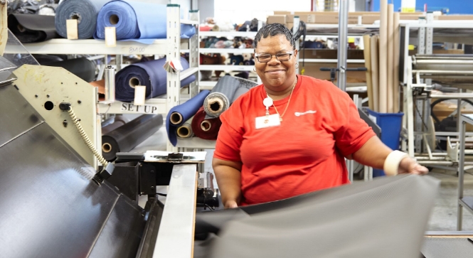  	A smiling female material handler spreads out a sheet of gray cloth.