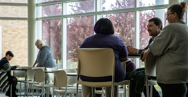 A group of five faculty members congregate and talk in a cafeteria setting.