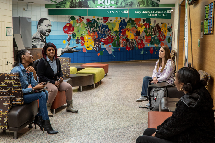 Four female Ivy Tech students talk as they sit on cushioned benches inside an academic building.