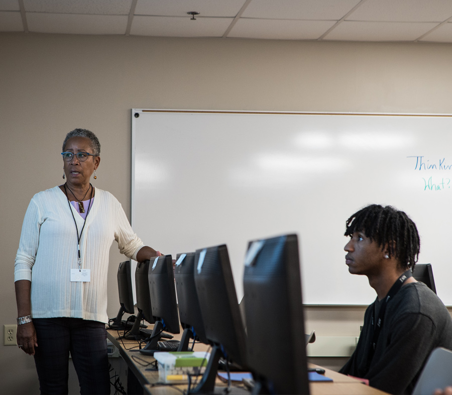 A male faculty member writes on the white board in the front of a classroom while students take notes.