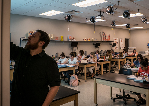 A male Ivy Tech faculty member writes on the board in a classroom while students take notes.