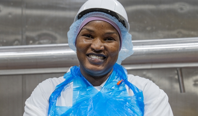 A Koch Foods employee in a hard hat and apron smiling about their job
