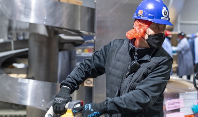 A Koch Foods employee in a hard hat and face mask working in a commercial cooking facility