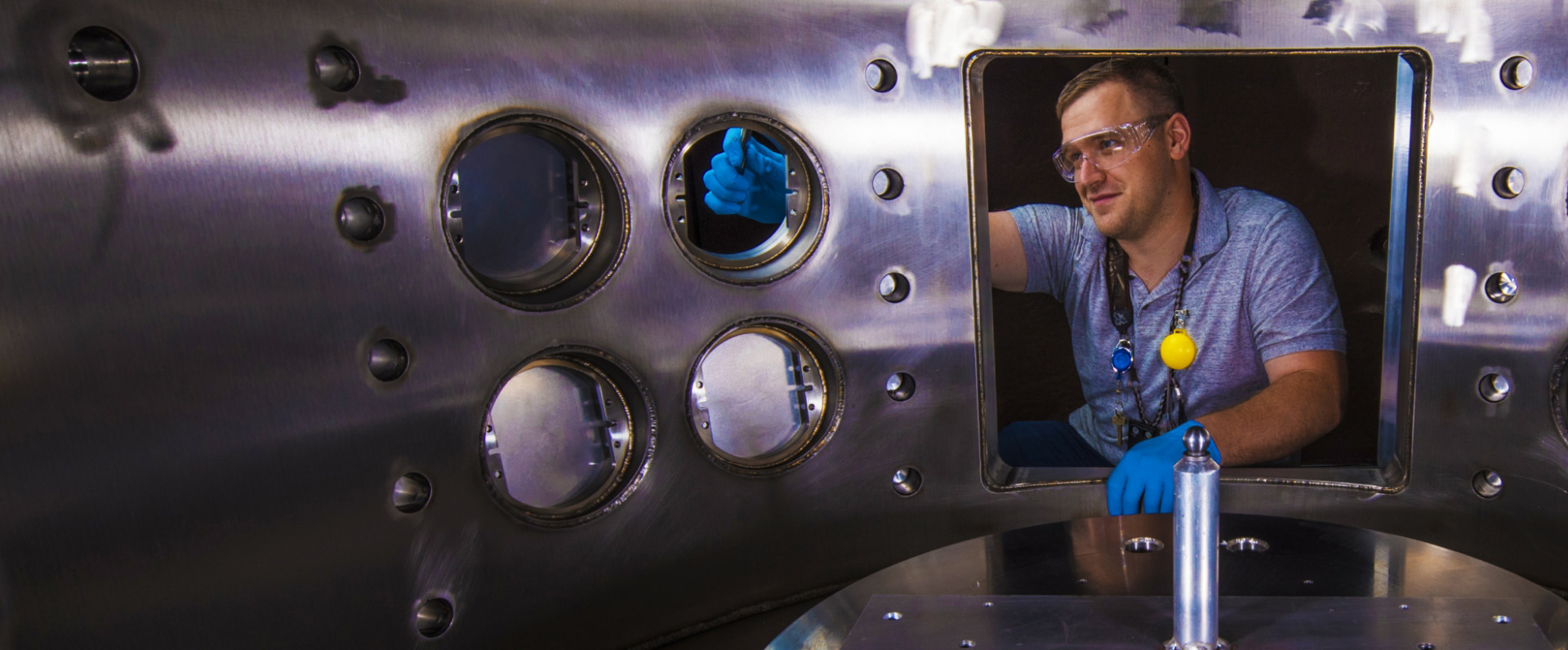 LANL engineer with safety goggles and gloves working on large metal frame.