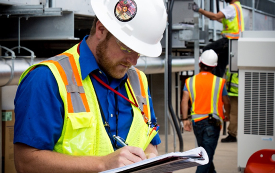 LANL employee wearing safety gear and writing in a notebook.