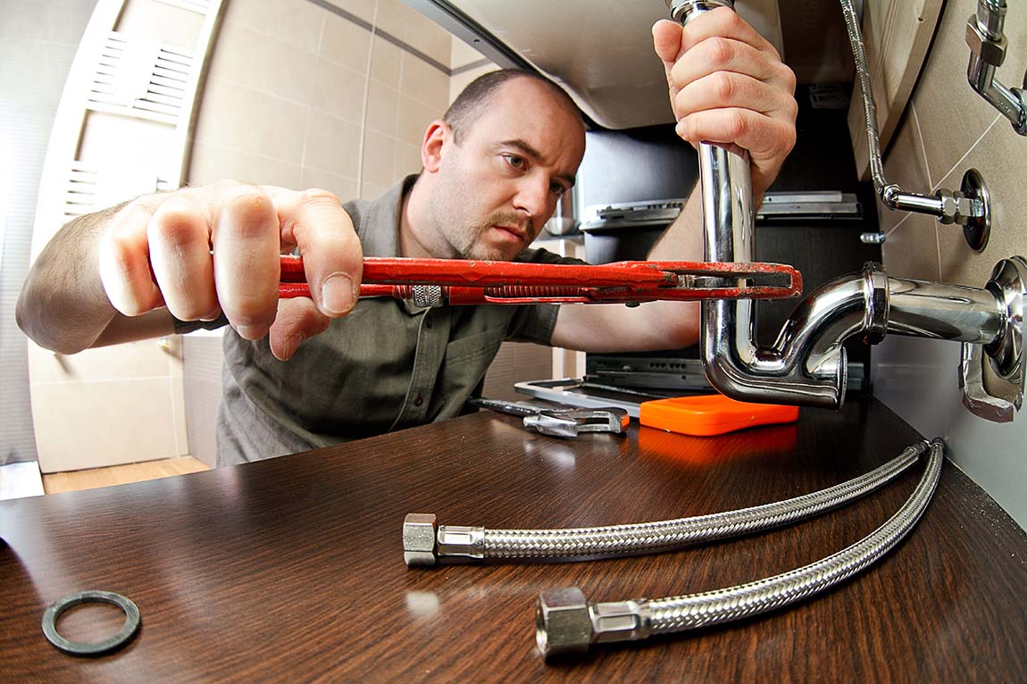 A maintenance staff member uses a wrench to adjust a pipe.