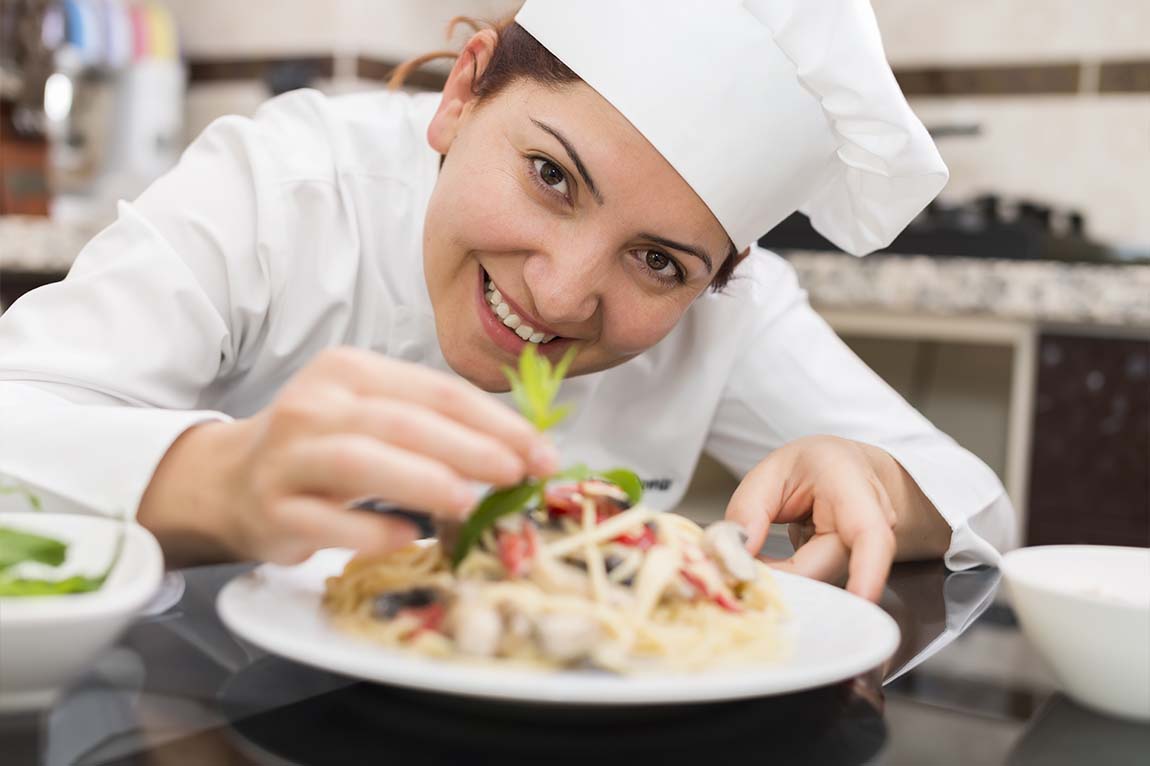 A smiling female cook puts the finishing touches on a delicious salad.