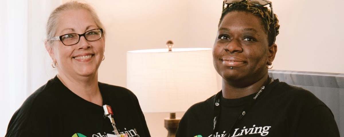 Two staff members in black Ohio Living t-shirts pause to smile during a productive workday.