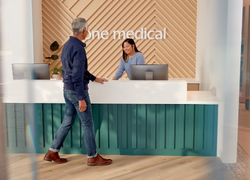 One Medical employee welcoming a patient at the front desk.