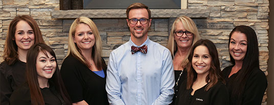 A male dentist stands with his staff of hygienists and dental assistants