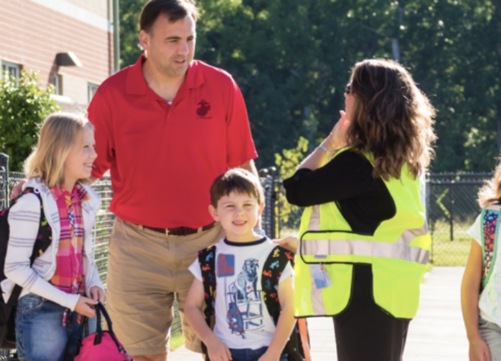 A bus safety assistant engaging in conversation with a father and his two children.